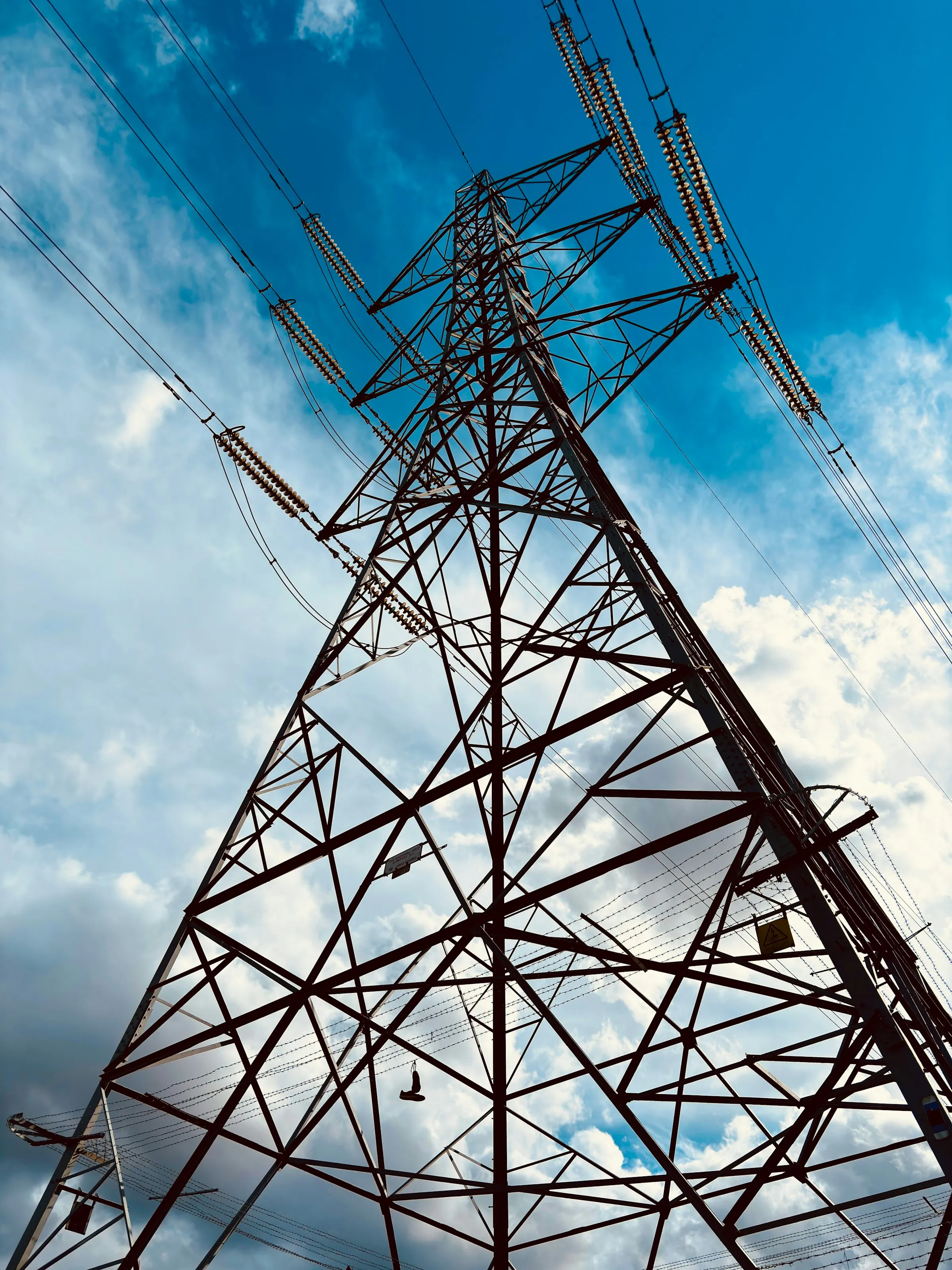Electricity transmission pylon viewed from below, blue sky.